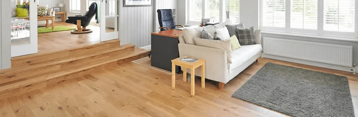 A modern living room with professionally installed laminate flooring, a beige sofa, a small side table, a gray rug, and large windows with white shutters in Irvine, CA